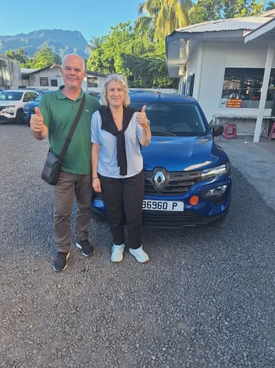 Couple de clients devant leur Renault Kwid bleue, pouces levés